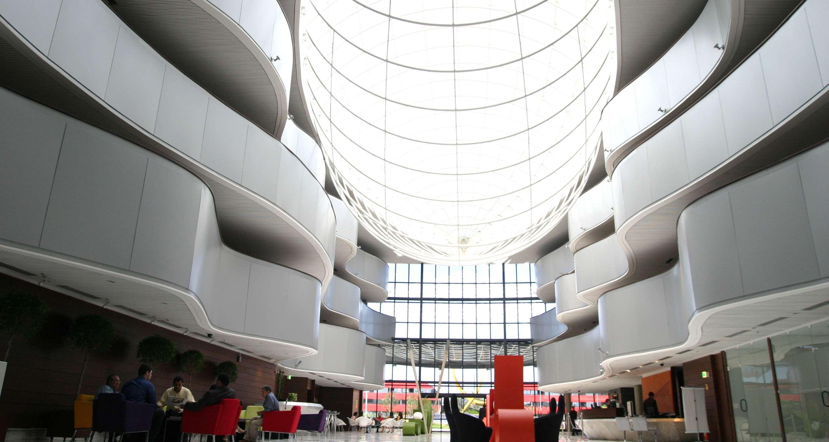 Отель Royal Tulip Brasilia Alvorada Экстерьер фото The photo depicts a modern interior space characterized by sleek, curvilinear architecture. The ceiling features a large, dome-like skylight that allows natural light to flood the area. The walls display a minimalist design with smooth, white surface